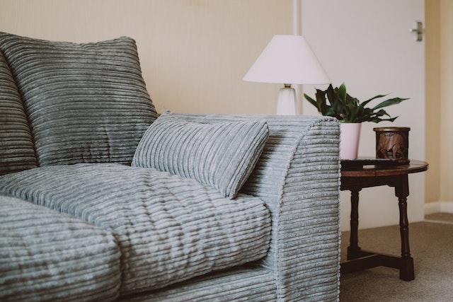 a blue-grey couch and dark wood side table in a white living room