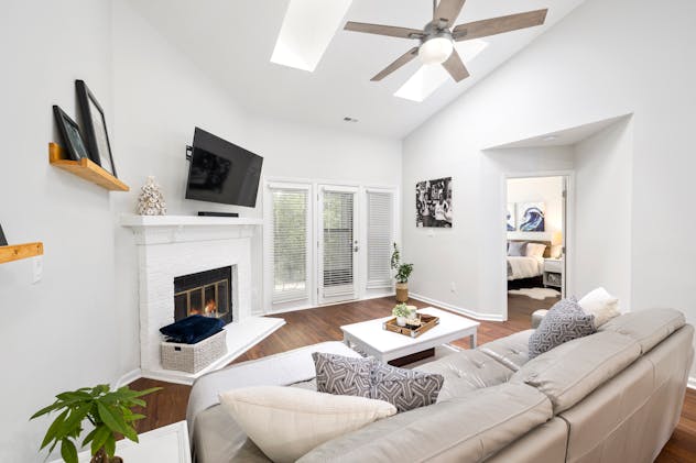 A white living room with grey furniture and a TV above the fireplace