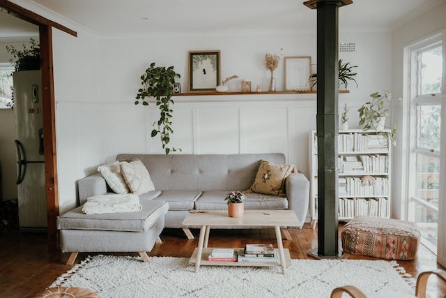 a small living room with a large window and a l-shaped grey couch